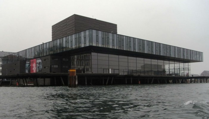 Das Royal Theater von Lundgaard & Tranberg Architects nimmt in seinem verglasten Obergeschoss, das Petrolgrün des Wassers auf und spiegelt durch die unregelmäßigen Kleinteiligkeit dieses Fensterbandes die Wellenstruktur wider