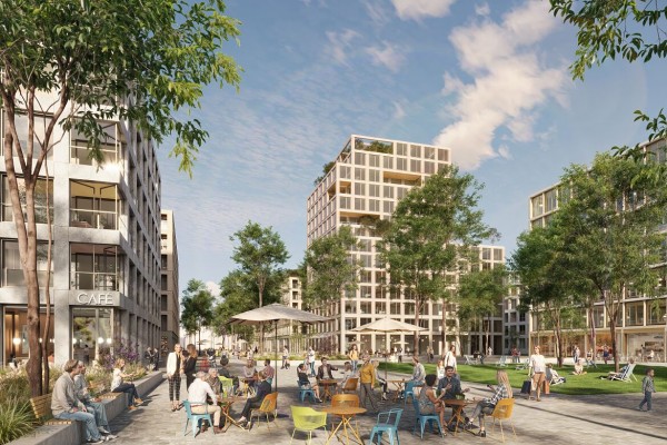 Bahnhofsplatz: Gebäude mit hellen Naturstein- und Rottönen vermitteln Offenheit und Wärme. Begrünte Dachterrassen und große Fensterflächen lassen das Areal freundlich und lebendig wirken.